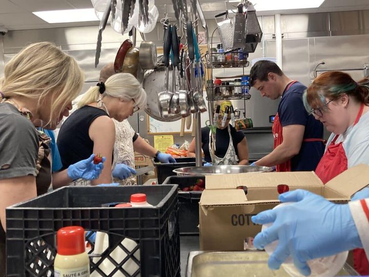 Volunteers in gloves pack food boxes in a community kitchen