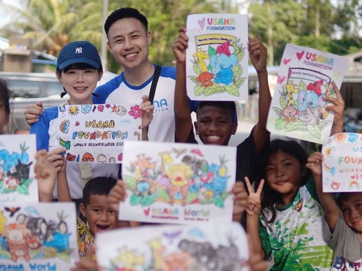 Children in Malaysia hold up their artwork with a USANA volunteer during World Service Week